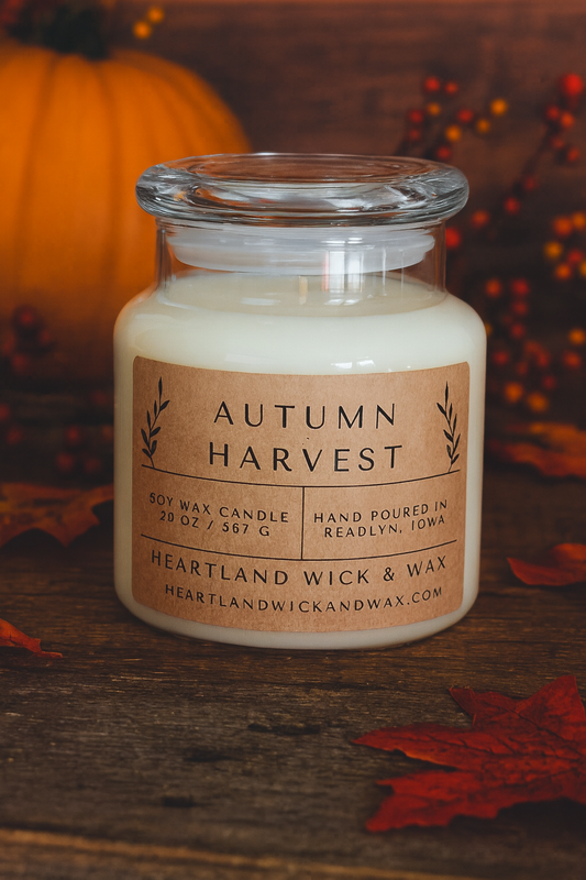 Candle in a glass jar labeled 'Autumn Harvest' with fall decorations in the background.